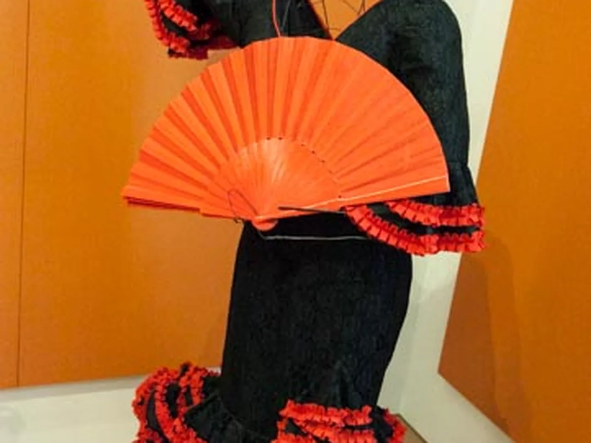 A traditional black and red flamenco dress with an orange fan on display